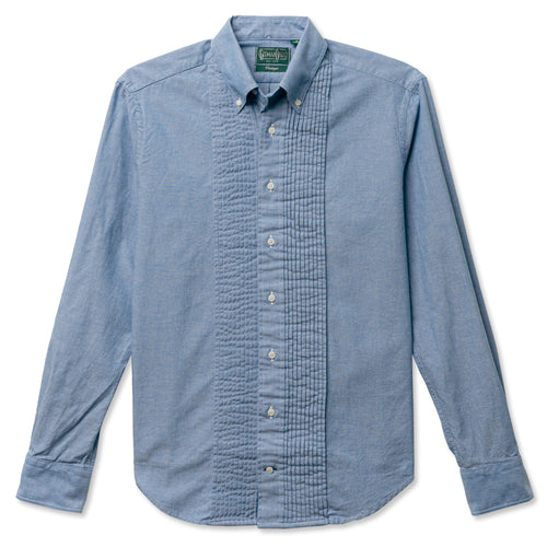 A blue button down tuxedo shirt with a chest pocket and a ruffled placket, made from a chambray fabric with white buttons.