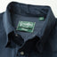 A close up photo of the navy button up collar, white pearl buttons green Gitman Vintage tag.